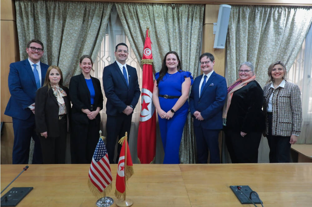A picture showing a group of College of Computing officials including Dean Marouane Kessentini pose for a  photo. Between them is a Tunisian flag. A table in front them has the USA and Tunisia Flag